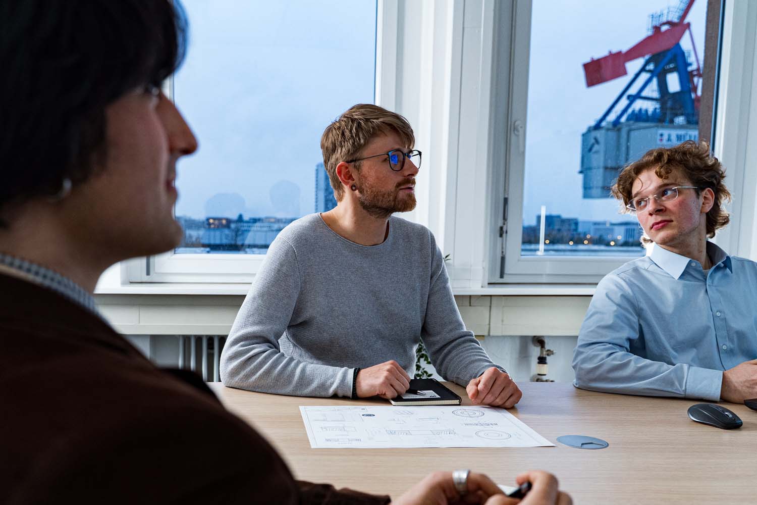 Drei Mitarbeiter an einem Tisch. Auf dem Tisch liegt der Ausdruck einer Konstruktionszeichnung.